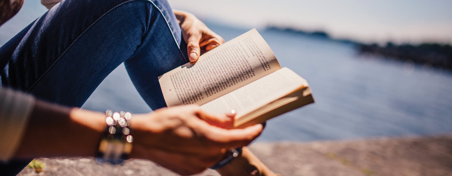 person reading a book by water 